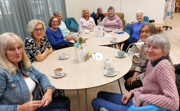 Nine ladies look to the camera while drinking coffee