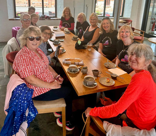 A group of ladies sit around a table with coffee and cake