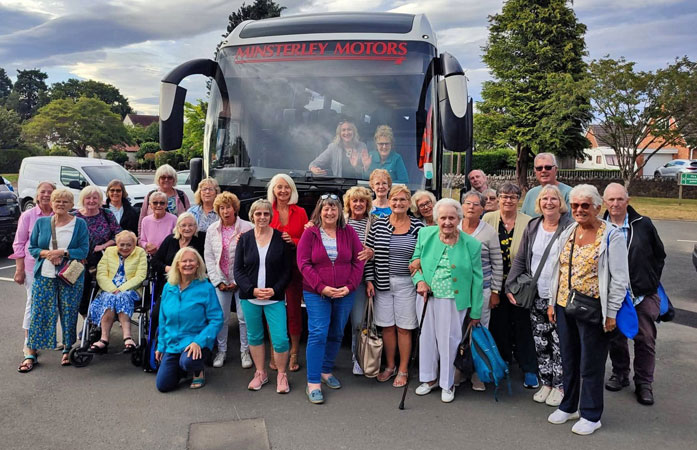 A large group of ladies and some men pose in front of a coach before travelling to Llandudno