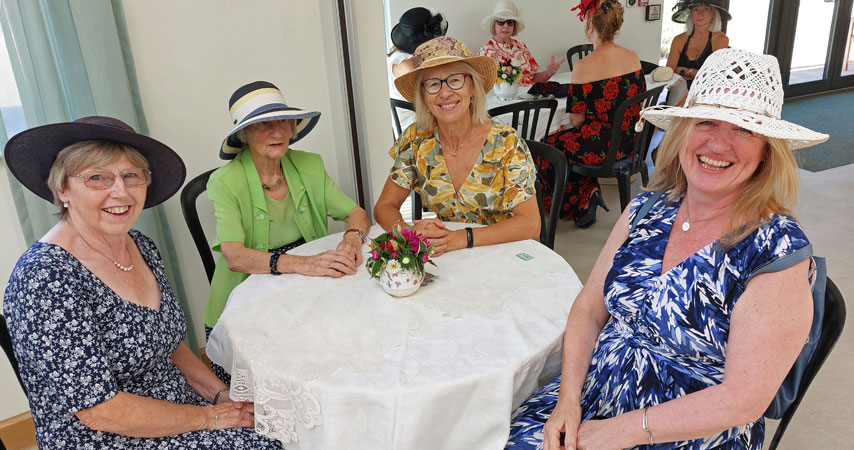Four ladies in hats sit around a table