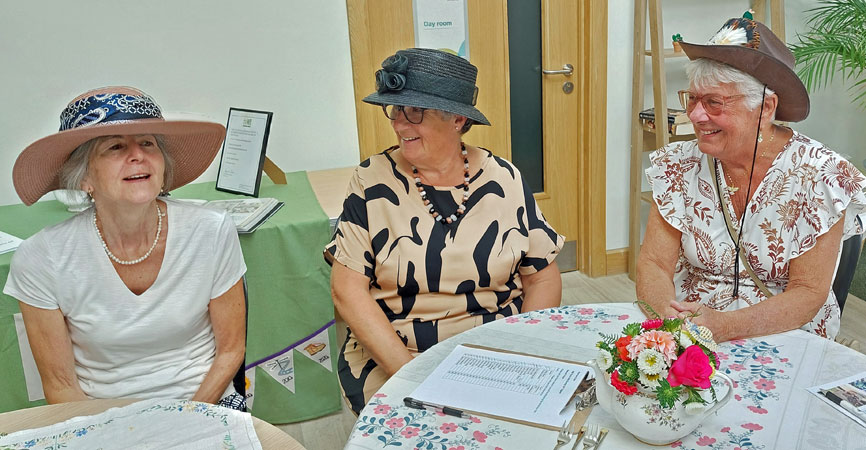 Three ladies in hats laugh 