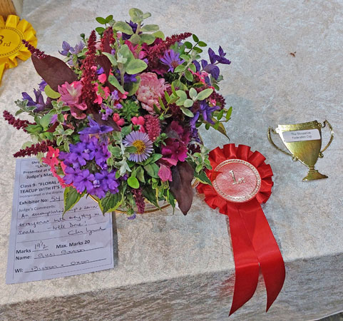 A flower arrangement with red winning rosette
