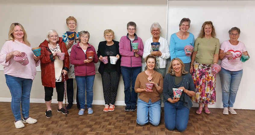 Twelve ladies pose for the camera holding pots they have painted